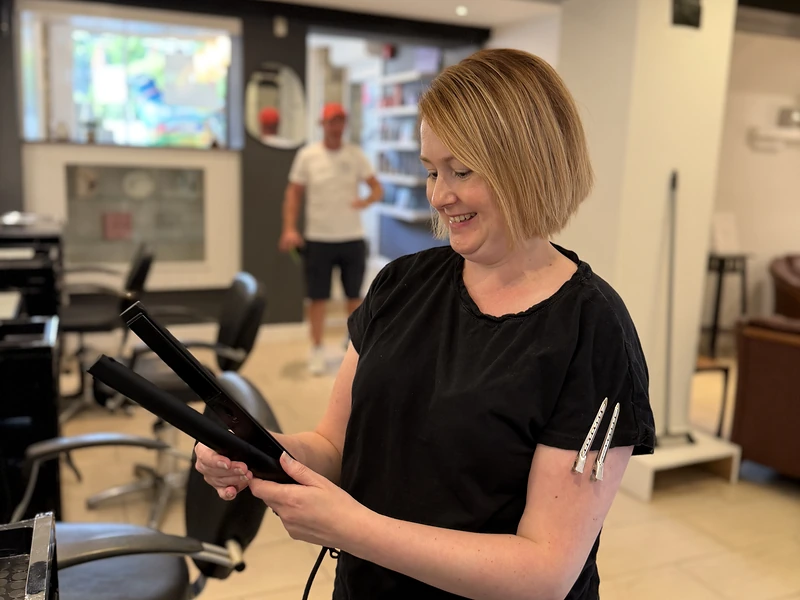 A smiling stylist checking a pair of hair straighteners inside Capillus Hair Salon