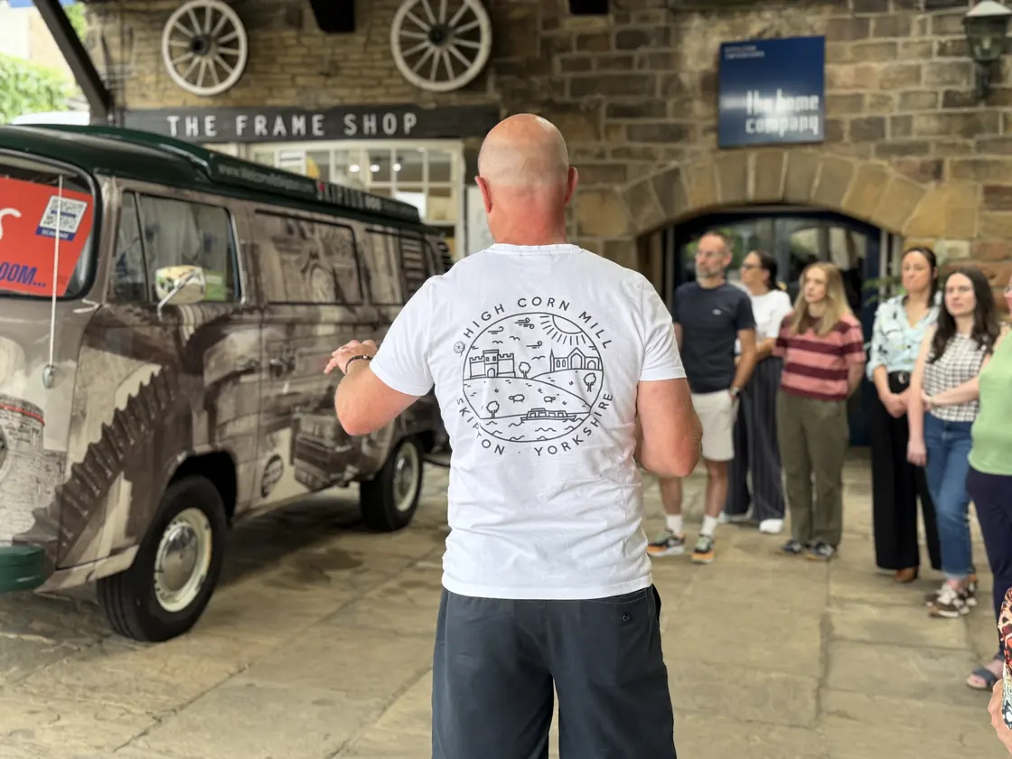 A guide talking to a tour group in the mill courtyard, beside the mill’s camper van
